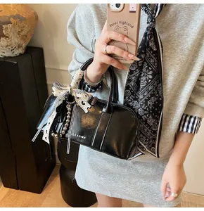 Detalle de bolso cilíndrico negro con lazo de encaje y colgante de cuentas plateadas