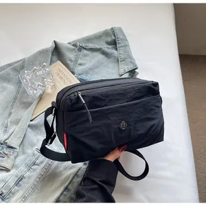 Detailansicht der schwarzen Nylon-Umhängetasche mit Doppelreißverschluss auf weißem Bett