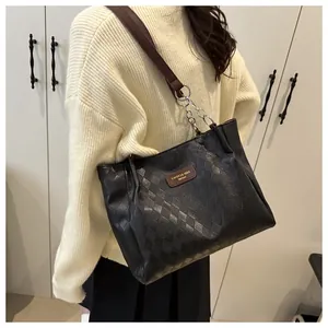 Detail of black quilted tote bag with chain strap and leather brand tag on shoulder