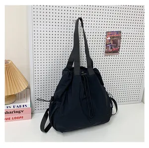 Detail van een zwarte nylon shopper met trekkoord en YUIX-zijlabel aan een gaatjesbord