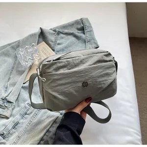 Detailansicht der grauen Nylon-Umhängetasche mit Metalllogo auf schlichtem Hintergrund