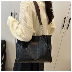 Detail of black quilted tote bag with brown straps and elegant gold chain hardware