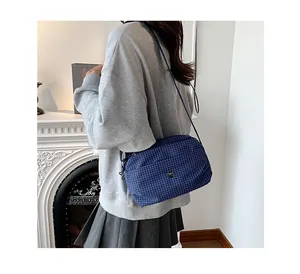 Détail d'un sac bandoulière en toile à carreaux bleus avec insigne en métal sur un mannequin
