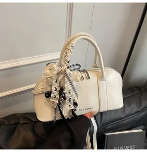 Detalle de bolso blanco semicilíndrico con encaje, lazos y cuentas plateadas elegantes