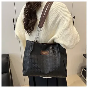Detail of black quilted tote bag with brown shoulder strap and chain accent on a model