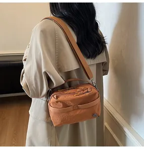 Close-up of orange-brown crossbody bag with wide strap on a model in trench coat