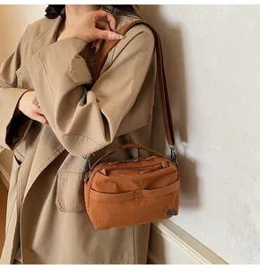 Detail of caramel brown nylon crossbody bag worn with khaki trench coat in soft light