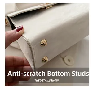 Détail des clous de protection dorés sur un sac à bandoulière en cuir ivoire