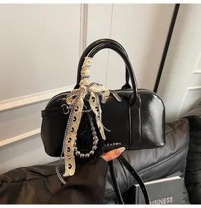 Detalle de bolso en cuero brillante negro con lazo de encaje y colgante de cuentas plateadas