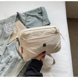 Nahaufnahme der beigen Nylon-Umhängetasche mit rundem Metall-Logo und Stoffdetails