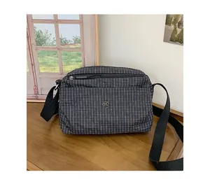 Détail du sac en toile à carreaux gris avec logo en métal et bandoulière réglable