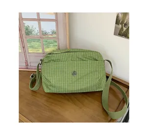 Détail du sac à bandoulière en toile à carreaux verts avec logo métallique et sangle réglable