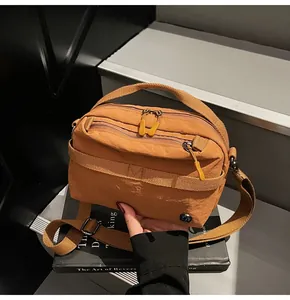 Detail of brown nylon crossbody bag featuring dual woven straps and multi-zipper layers