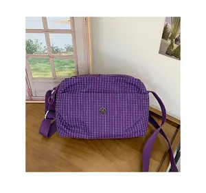 Détail du sac en toile à carreaux violets avec logo en métal et bandoulière réglable