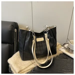 Detail of black quilted tote bag with silver chain strap and brand tag on fabric background
