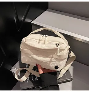 Detail view of white nylon crossbody bag with dual zippers and textured fabric finish