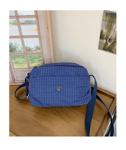 Détail du sac bandoulière à carreaux bleus avec logo en métal et sangle réglable