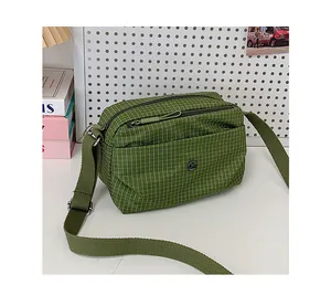 Vue détaillée du sac bandoulière en toile à carreaux vert herbe avec logo métallique