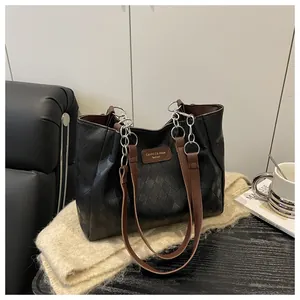 Close-up of black quilted tote bag with chain strap and brown leather logo tag detail
