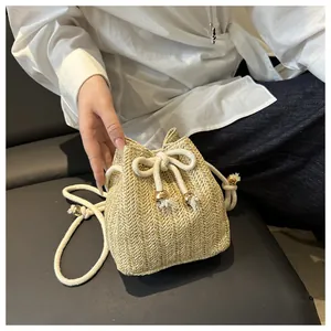Dettaglio della borsa a secchiello intrecciata beige con motivo a spina di pesce e sfera oro