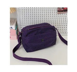 Détail du sac bandoulière en toile à carreaux violets avec logo et double fermeture éclair