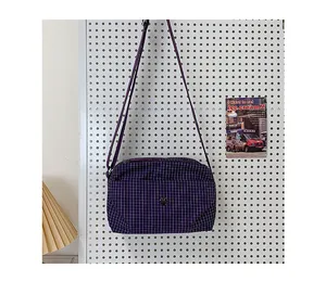 Vue détaillée du sac bandoulière en toile à carreaux violets avec logo en métal sur support