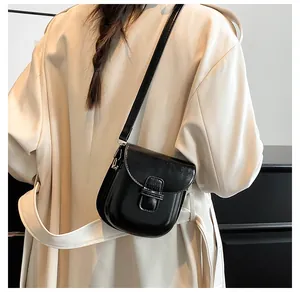 Dettaglio di una borsa a tracolla nera a sella abbinata a un trench coat beige elegante