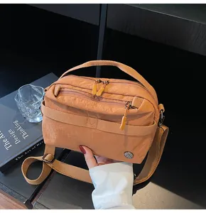 Macro shot of a tan nylon crossbody bag with zipper layers on a desk setup