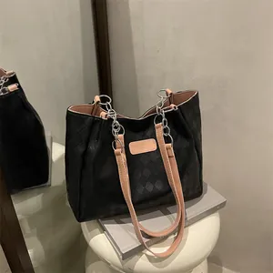 Large black quilted leather tote bag with silver chain straps on a white stool