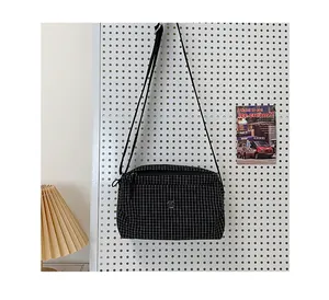 Détail du sac bandoulière en toile à carreaux suspendu sur un panneau perforé blanc