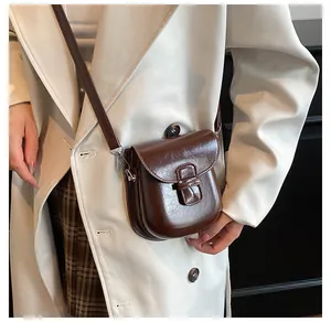 Dettaglio della borsa a tracolla vintage in pelle cerata marrone indossata da un modello