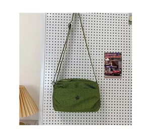 Détail du sac à bandoulière en toile à carreaux verts avec sangle réglable et logo