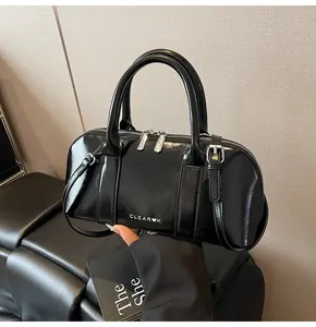 Detalle de un bolso Boston de charol negro con cremalleras plateadas y logo Clear K