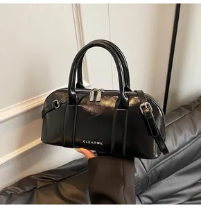 Detalle de un bolso Boston negro brillante con herrajes plateados y correa ajustable