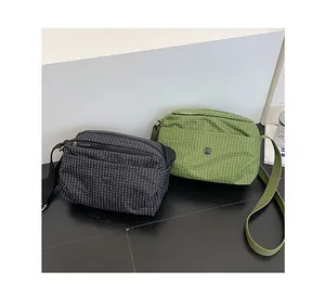 Détail de sacs bandoulière en toile à carreaux noir et vert avec logo métallique rond