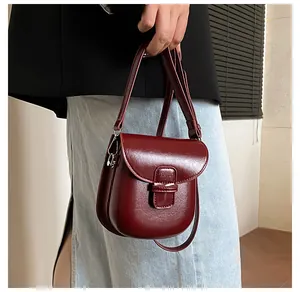 Dettaglio di una piccola borsa a tracolla rosso scuro lucida con ganci argento