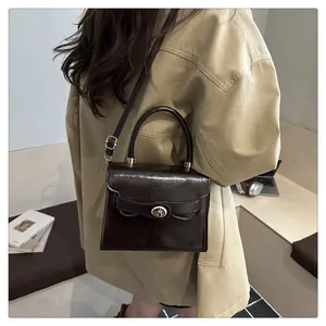 Dettaglio borsa in pelle marrone lucida con chiusura a scatto dorata e manico
