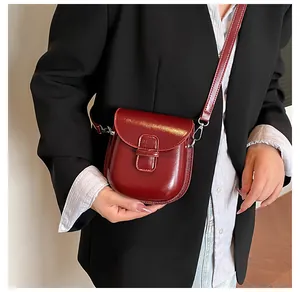 Dettaglio di una borsa a tracolla in pelle lucida rosso scuro indossata su un blazer nero