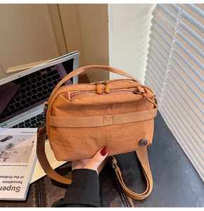 Close-up of orange nylon crossbody bag with pleated texture and stylish multi-zipper design