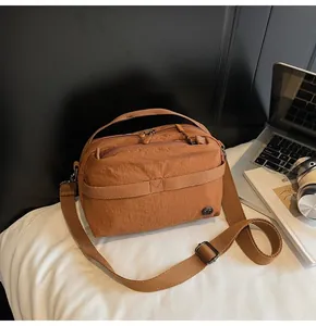 Detail view of caramel brown pleated nylon crossbody bag with dual zipper compartments