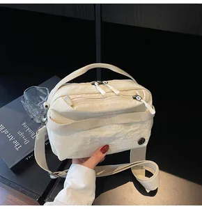 Detail of off-white crossbody bag with wrinkled texture, dual zippers, and wide strap