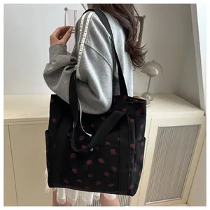 Black corduroy tote bag featuring red strawberry prints shown on a female model shoulder