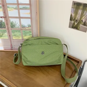Sac bandoulière en toile à carreaux verts avec logo M en métal sur table en bois