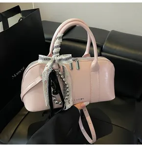 Detalle de bolso cilíndrico rosa con lazo y logo LEAR K sobre un sofá de cuero negro
