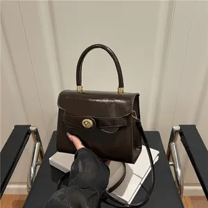 Borsa a mano minimalista in pelle verniciata marrone con chiusura dorata sulla sedia