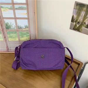 Sac à bandoulière en toile à carreaux violets avec logo argenté sur table en bois