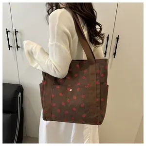 Close-up of strawberry print corduroy tote bag worn by a model in a modern interior