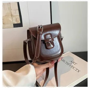 Dettaglio di una mini borsa a tracolla marrone scuro lucida accanto a libri d'arte moderni