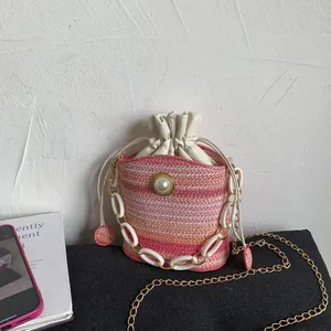 Gradient woven bucket bag with pearl detail and dual straps on a display surface
