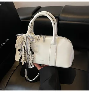 Primer plano del bolso Boston de cuero blanco con colgante de lazo y logo CLEARCK